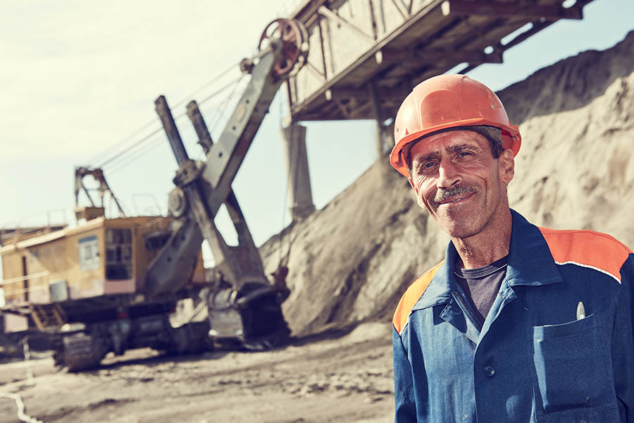 Mining Insurance - Mining Worker Standing in Front of a Heavy Excavator Loading Gravel into a Train Container