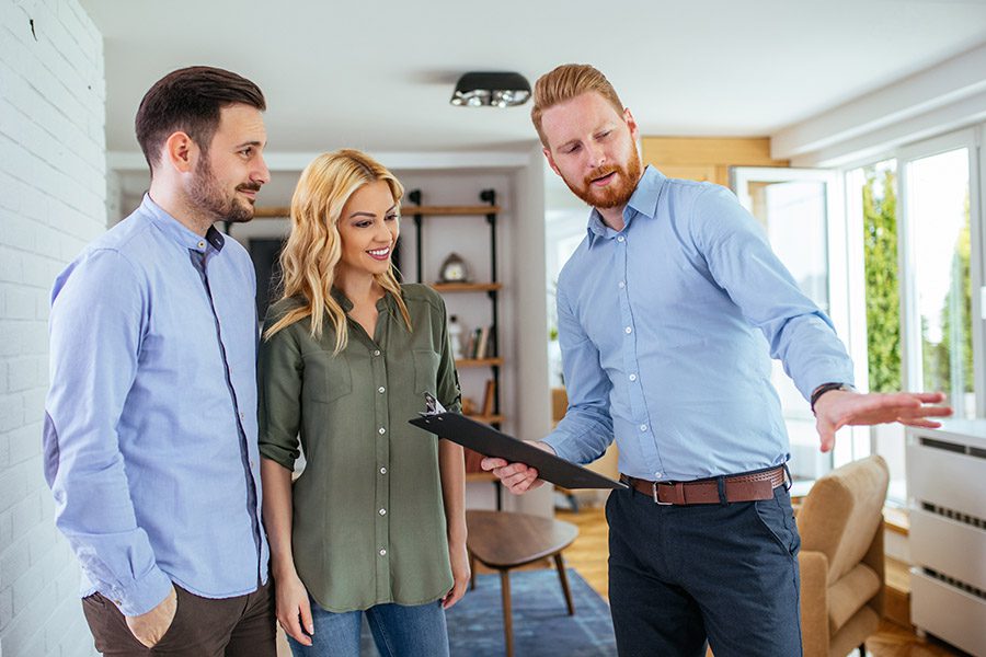 Business Insurance - Realtor Holding a Clipboard Showing the Interior of a Home to a Happy Couple