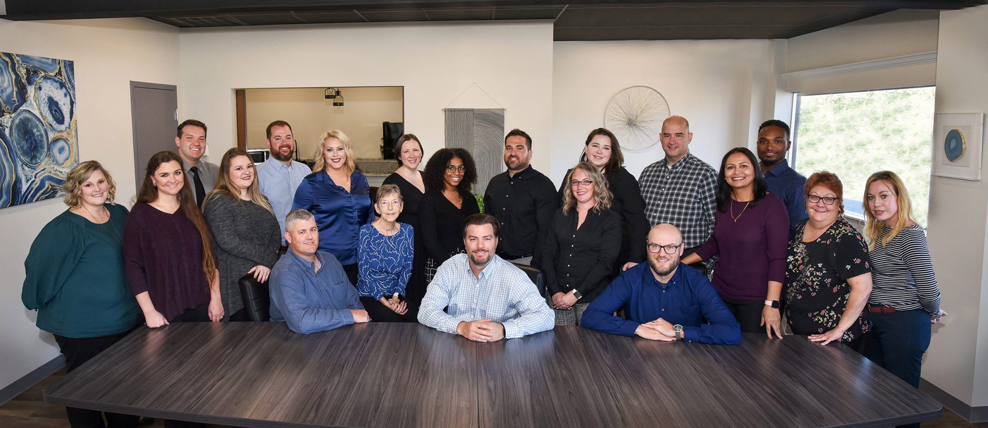 Homepage - Group Shot of Commonwealth Insurance Services Team Sitting and Standing Together Near a Long Conference Table in Their Office