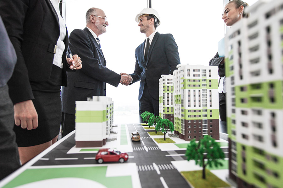 Specialized Business Insurance - An Investor and an Architect Smile and Shake Hands During After a Presentation of a Development Project Displaying Scaled Down Model of Buildings